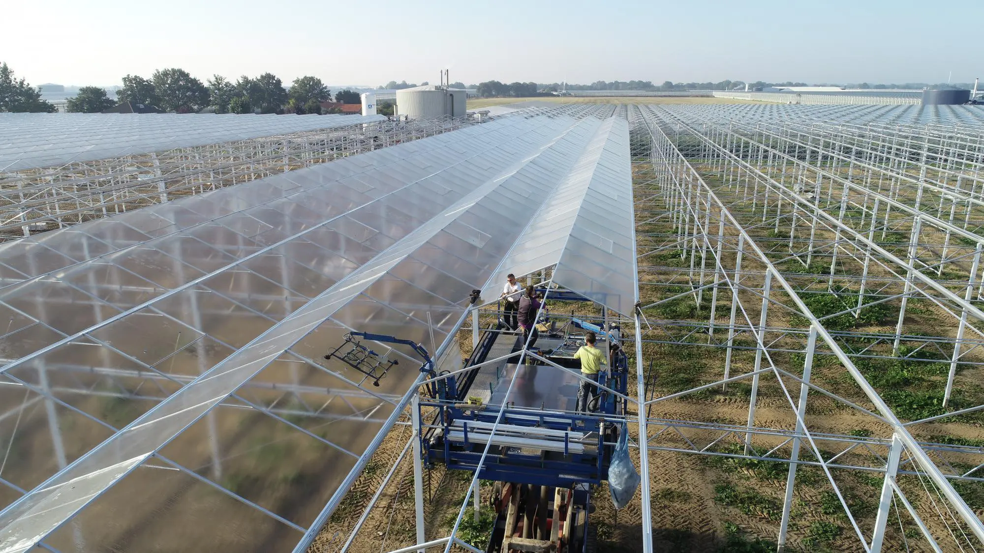 Roof glazing machine with a vacuum lifter working along a Venlo roof, panes going into one bay while the next still stands open