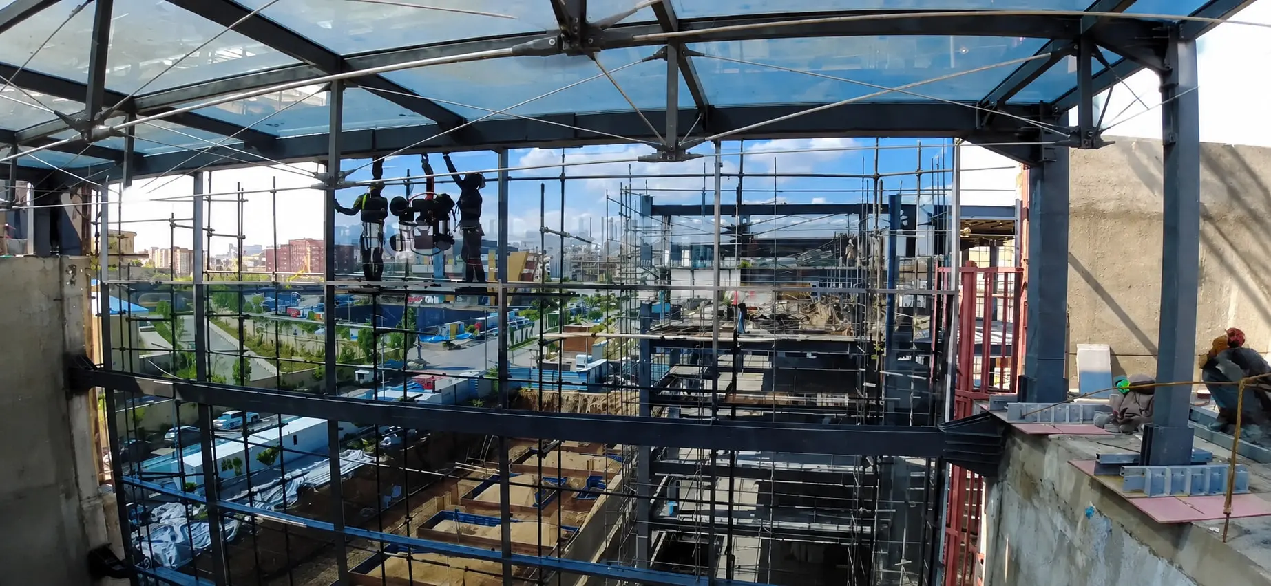 Glazing being installed at the edge of a Fanap courtyard roof from a platform over the open courtyard, the roof steel landing on its own column