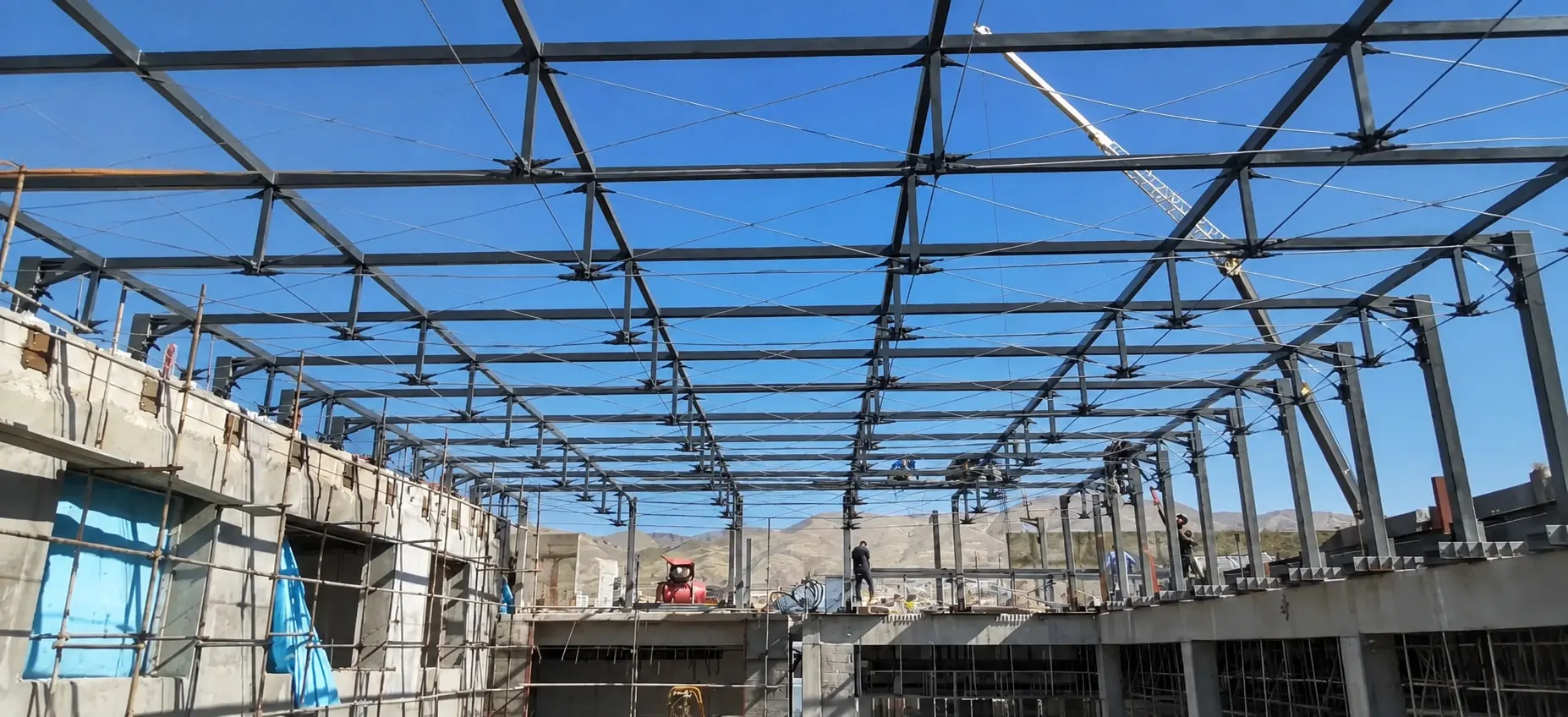 A Fanap courtyard roof under erection — the steel grid in place, a strut under each node and the tie rods between them