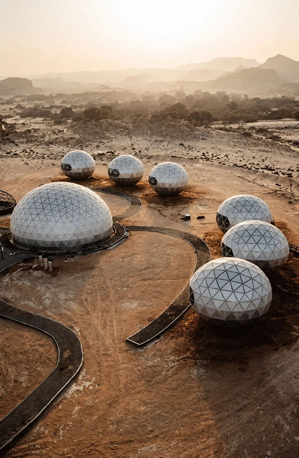 Geodesic resort units set across arid ground in low afternoon light, linked by curving paths, with escarpments beyond