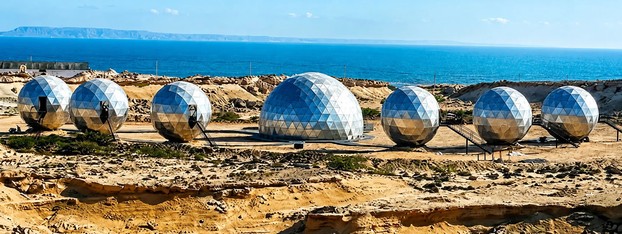 A row of CORTEX geodesic resort units on the coast, each shell delivered as one structural and envelope package