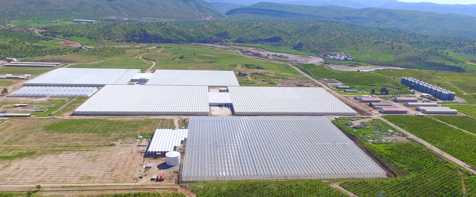 The full greenhouse estate in its valley, with service buildings and water storage