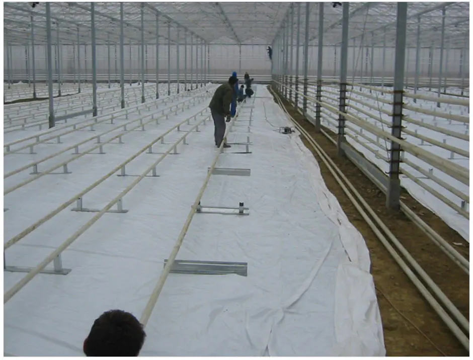 Installers laying ground cover and pipe rail between cultivation beds inside a finished greenhouse