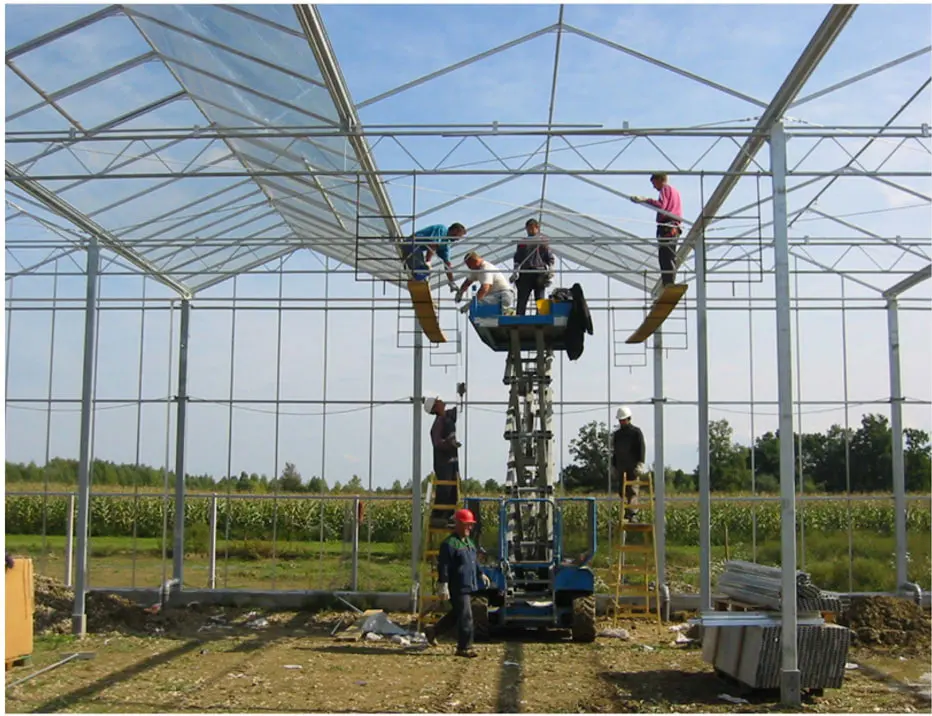Glazing crew working from a lift platform inside a partially glazed Venlo greenhouse frame