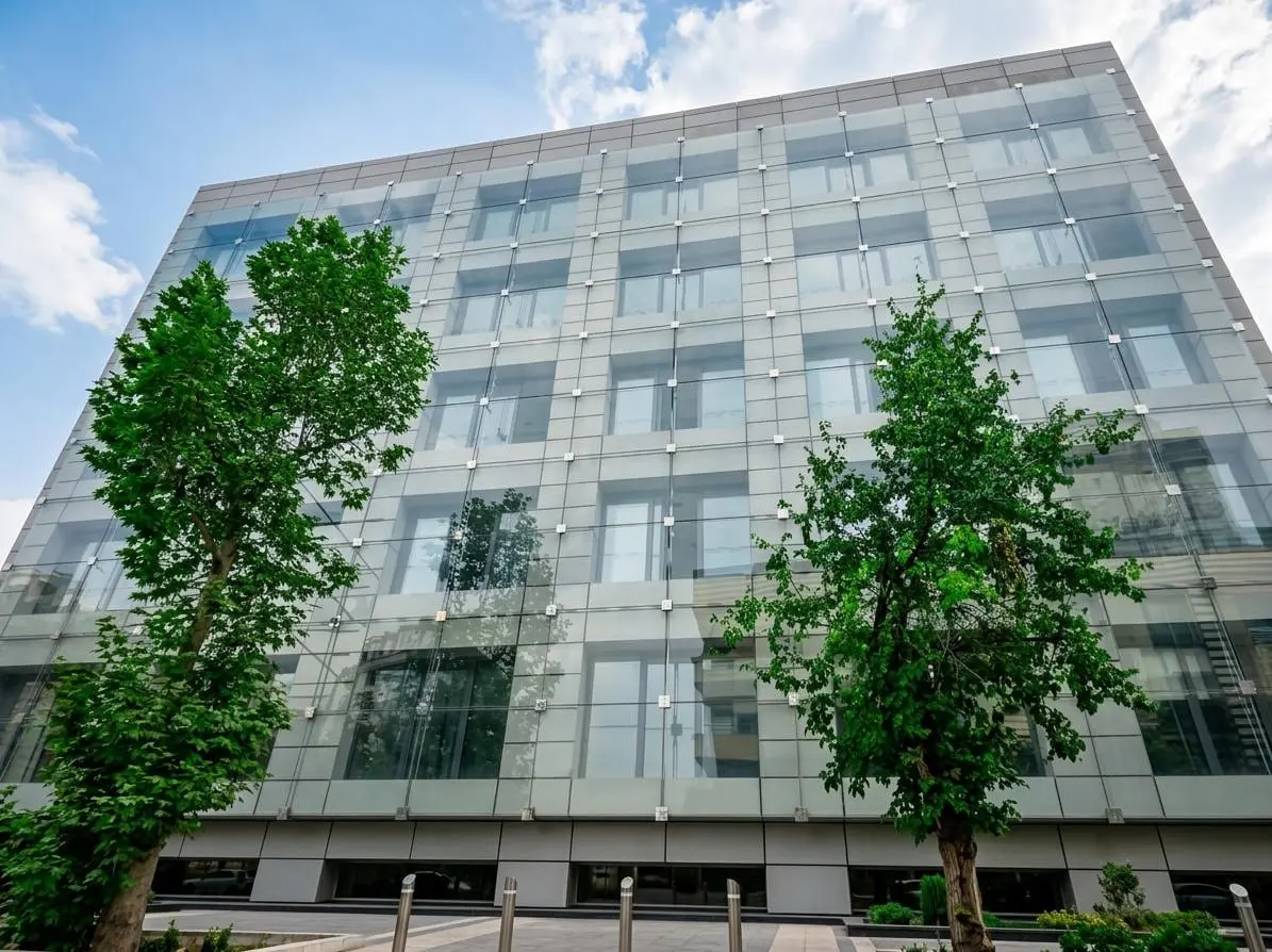 Moghaddas Ardebili Office, Tehran — the glazed cable-net wall to the street elevation, seen from below between two trees