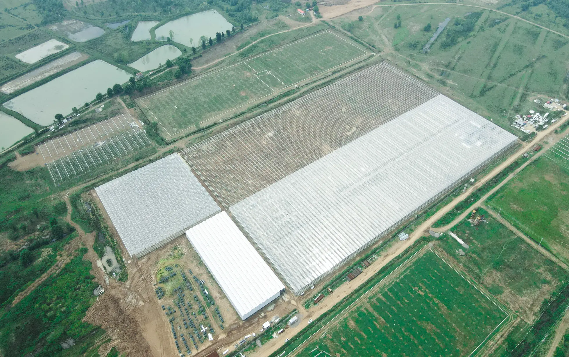 Aerial view of a completed Venlo glass greenhouse block set among cultivated fields at Siahkal, Gilan